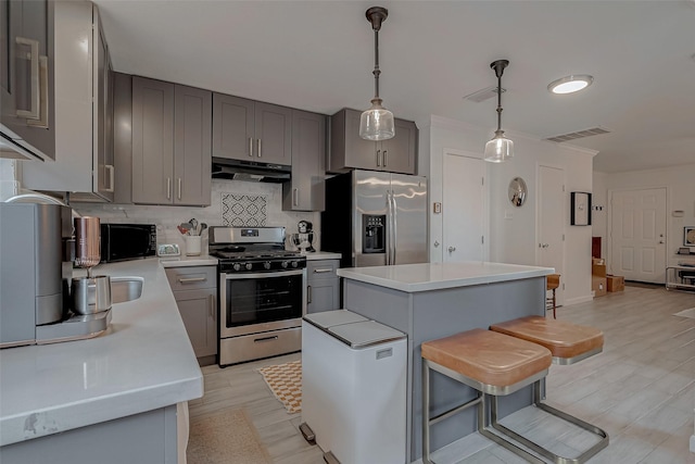 kitchen with a kitchen bar, gray cabinetry, a kitchen island, pendant lighting, and stainless steel appliances