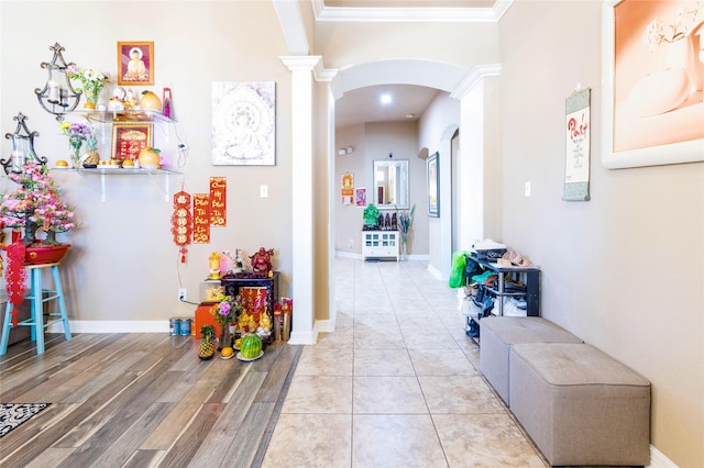 hall with decorative columns, crown molding, and light wood-type flooring