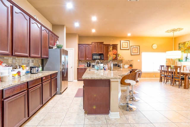 kitchen with a kitchen breakfast bar, range, light stone counters, stainless steel fridge with ice dispenser, and a center island with sink