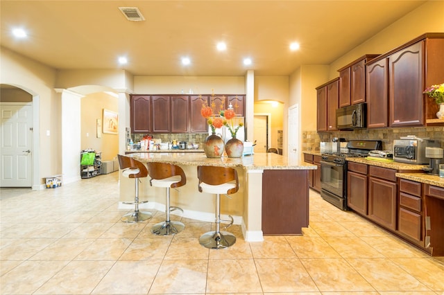 kitchen featuring light tile patterned floors, a breakfast bar, light stone counters, black appliances, and a kitchen island