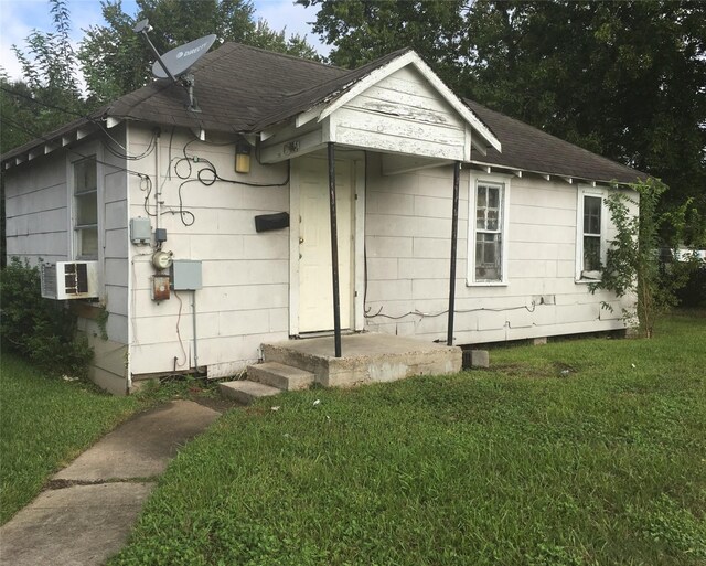 view of front of home with a shingled roof, cooling unit, and a front yard