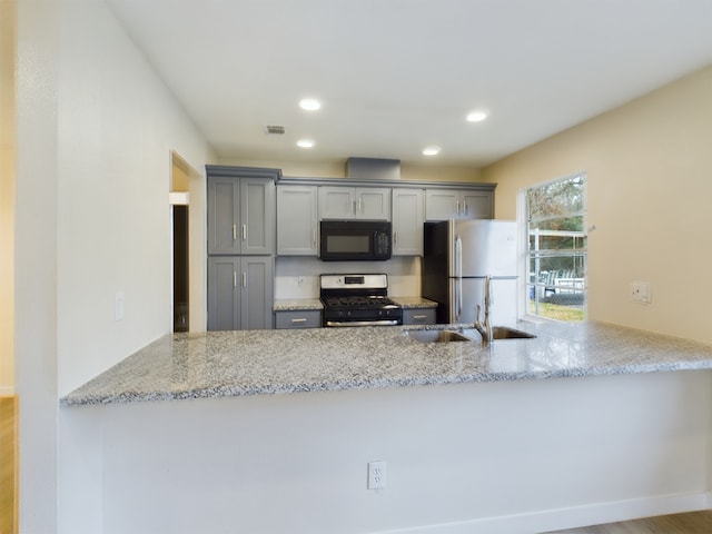 kitchen with a peninsula, gray cabinetry, appliances with stainless steel finishes, and a sink