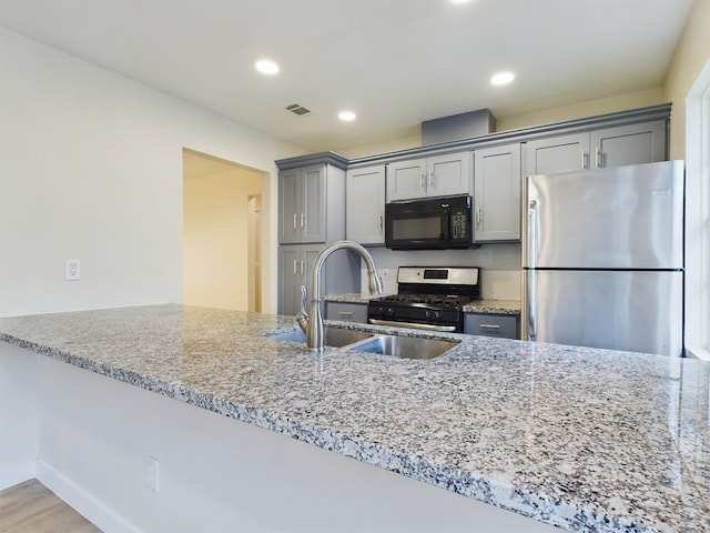 kitchen with light stone counters, gray cabinetry, stainless steel appliances, and a sink