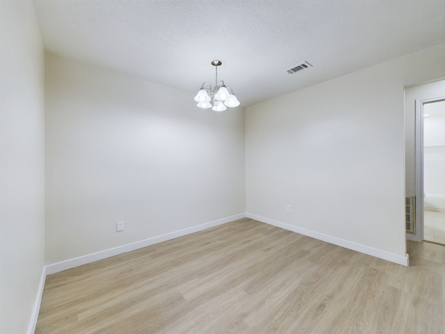 unfurnished room featuring a chandelier, visible vents, light wood-type flooring, and baseboards