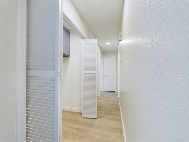 corridor with a textured wall, baseboards, and light wood finished floors