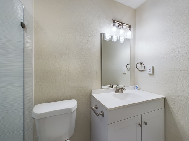 bathroom with toilet, vanity, and a textured wall