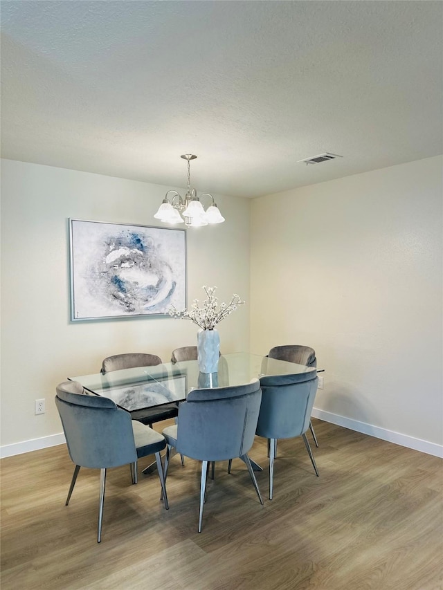 dining room featuring visible vents, wood finished floors, baseboards, and a chandelier