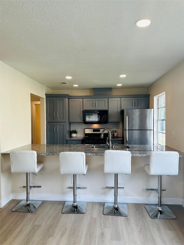 kitchen with a kitchen breakfast bar, gray cabinets, and appliances with stainless steel finishes