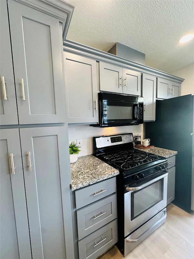 kitchen featuring gray cabinetry, black microwave, stainless steel gas range, light stone counters, and a textured ceiling