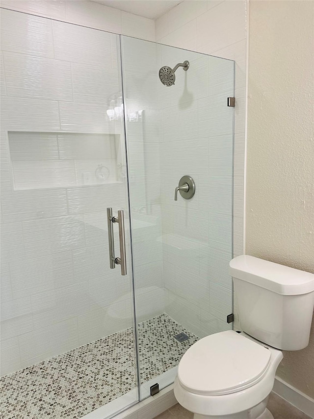 bathroom featuring toilet, a shower stall, and a textured wall