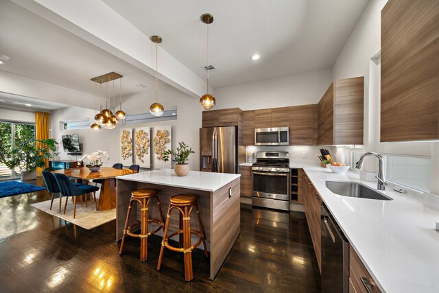 kitchen with sink, stainless steel appliances, a center island, a kitchen bar, and decorative light fixtures