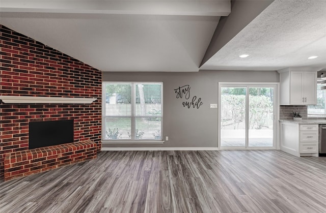 unfurnished living room with a fireplace, vaulted ceiling, a textured ceiling, and light wood-type flooring