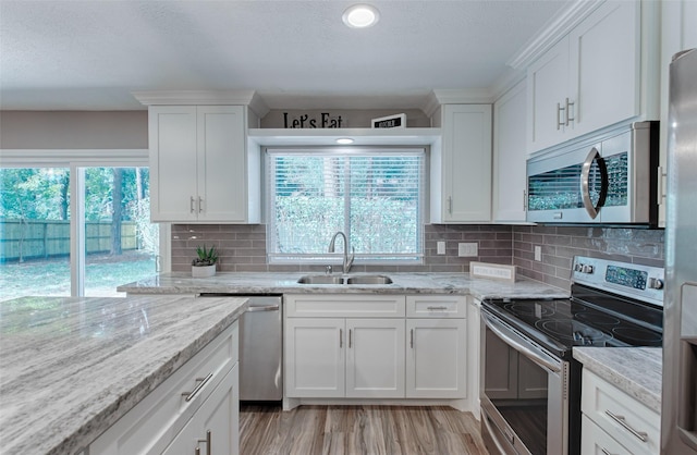 kitchen with stainless steel appliances, white cabinetry, light stone countertops, and sink