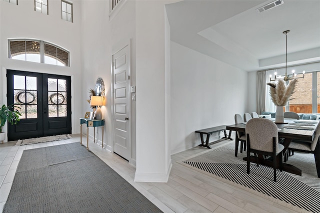 entrance foyer with french doors, a tray ceiling, a notable chandelier, a towering ceiling, and light hardwood / wood-style floors