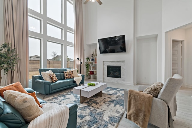 living area with light wood-type flooring, a high ceiling, a ceiling fan, and a glass covered fireplace