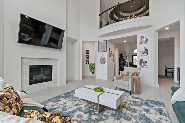 living room with a glass covered fireplace, a towering ceiling, baseboards, and wood finished floors