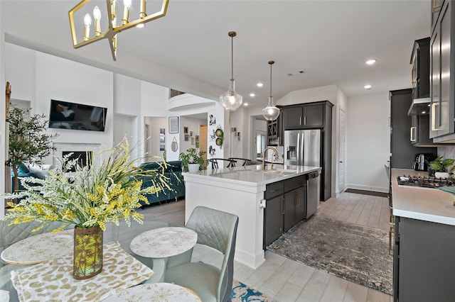 kitchen with appliances with stainless steel finishes, decorative light fixtures, light hardwood / wood-style floors, and a center island with sink