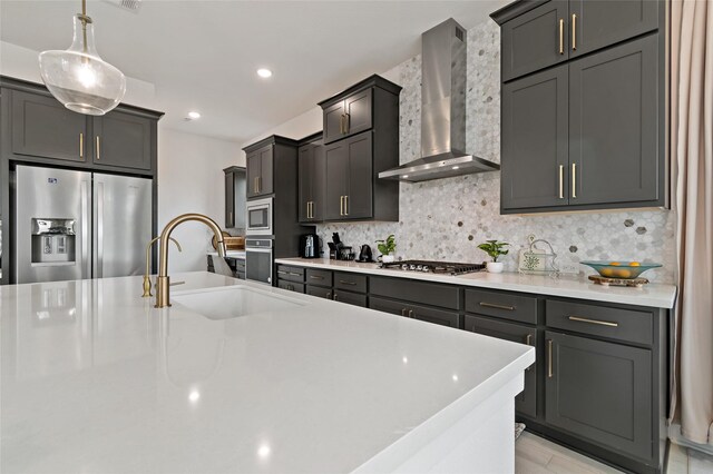 kitchen featuring sink, hanging light fixtures, appliances with stainless steel finishes, wall chimney range hood, and backsplash