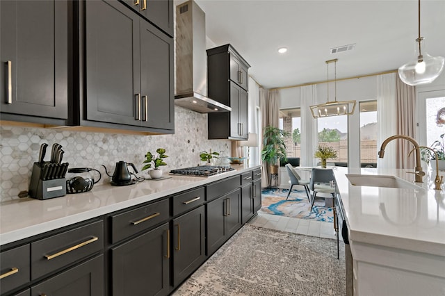 kitchen featuring pendant lighting, stainless steel gas stovetop, sink, plenty of natural light, and wall chimney range hood