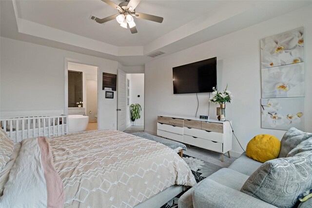 carpeted bedroom with a raised ceiling, ceiling fan, and ensuite bath