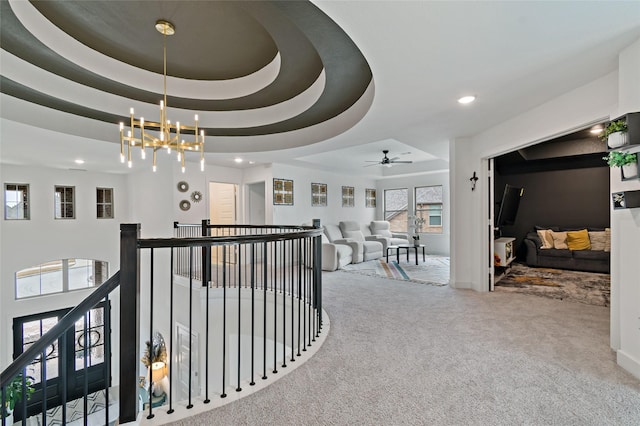 hallway with an inviting chandelier, a tray ceiling, and carpet floors