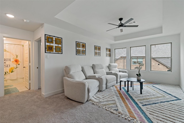 living room with ceiling fan, visible vents, baseboards, carpet, and a raised ceiling