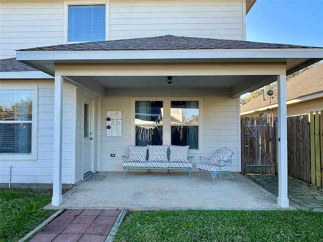 view of exterior entry featuring fence, covered porch, and a shingled roof