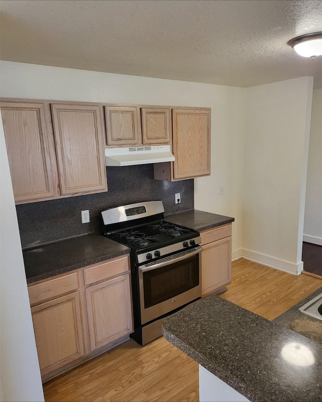 kitchen featuring stainless steel range with gas stovetop, a textured ceiling, light brown cabinets, and light hardwood / wood-style floors