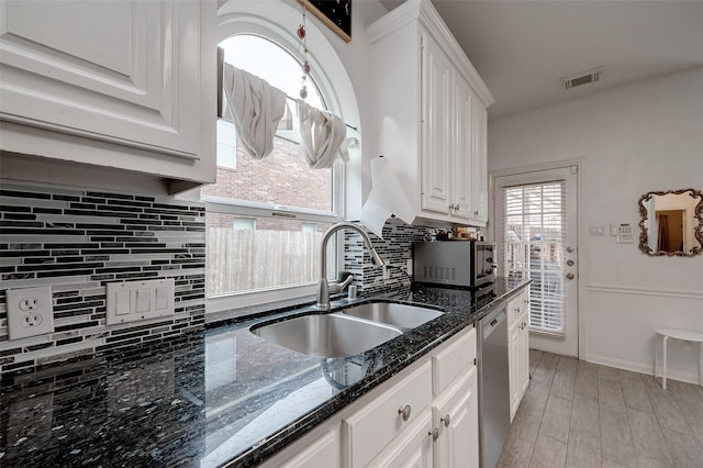 kitchen featuring sink, appliances with stainless steel finishes, dark stone counters, decorative backsplash, and white cabinets