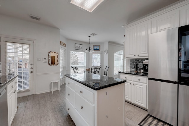 kitchen with white cabinetry, dark stone countertops, stainless steel appliances, a center island, and decorative light fixtures