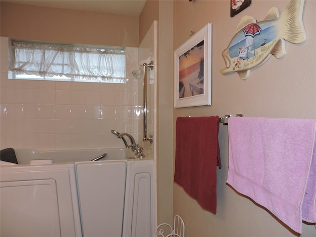 bathroom featuring washer / clothes dryer and a tub to relax in