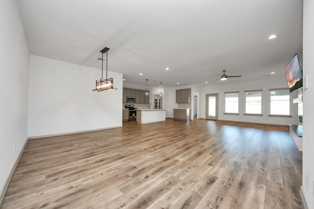 unfurnished living room featuring ceiling fan with notable chandelier and light hardwood / wood-style floors