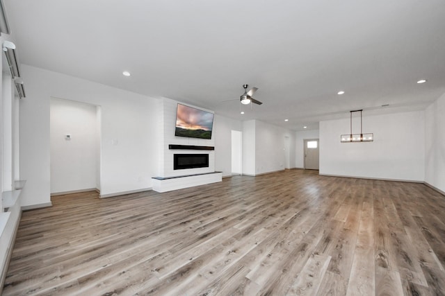 unfurnished living room featuring a large fireplace, ceiling fan, and light hardwood / wood-style flooring