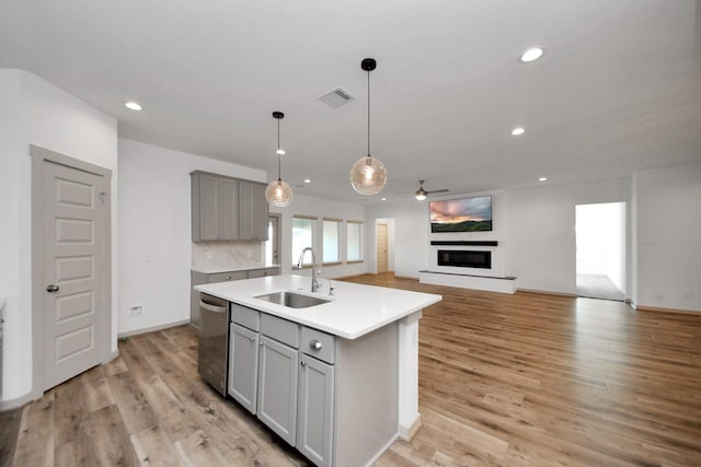 kitchen with gray cabinets, dishwasher, sink, a center island with sink, and light hardwood / wood-style flooring