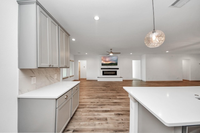 kitchen featuring gray cabinetry, decorative backsplash, hanging light fixtures, ceiling fan, and light hardwood / wood-style floors