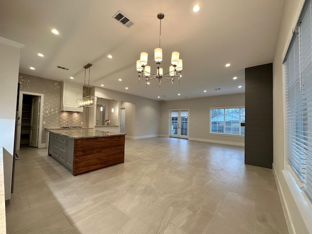 kitchen with hanging light fixtures, a notable chandelier, light stone countertops, white cabinets, and a kitchen island