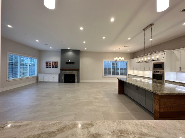 kitchen featuring stone countertops, pendant lighting, a fireplace, white cabinets, and stainless steel appliances