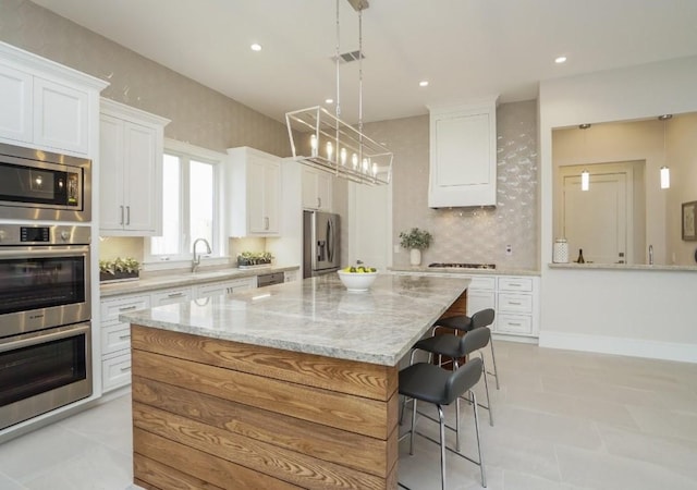 kitchen with light stone counters, decorative light fixtures, a center island, appliances with stainless steel finishes, and white cabinets