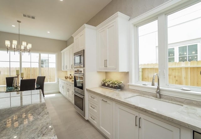 kitchen with white cabinetry, sink, light stone counters, and decorative light fixtures