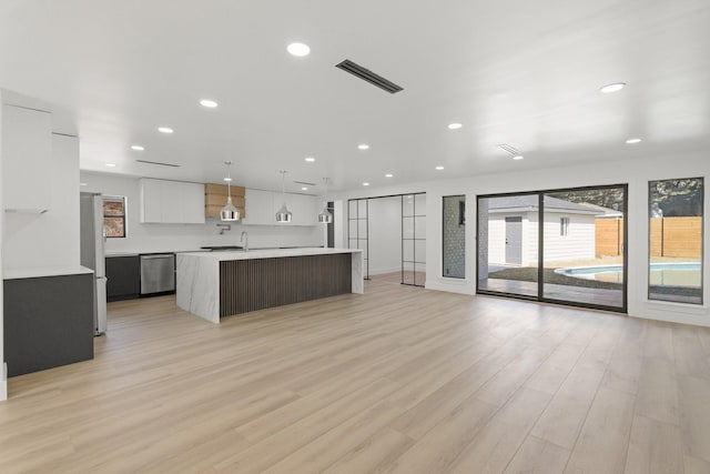 kitchen featuring appliances with stainless steel finishes, decorative light fixtures, white cabinets, a center island with sink, and light wood-type flooring