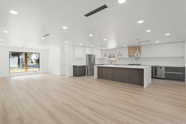 kitchen with pendant lighting, stainless steel appliances, beverage cooler, a kitchen island with sink, and white cabinets