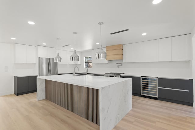 kitchen featuring wine cooler, stainless steel fridge, an island with sink, and white cabinets