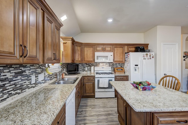 kitchen featuring a kitchen island, sink, backsplash, light stone counters, and white appliances