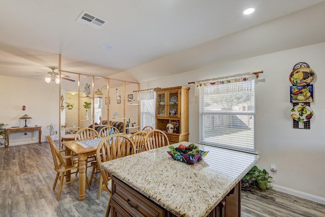 kitchen with hardwood / wood-style floors, light stone countertops, a center island, and ceiling fan