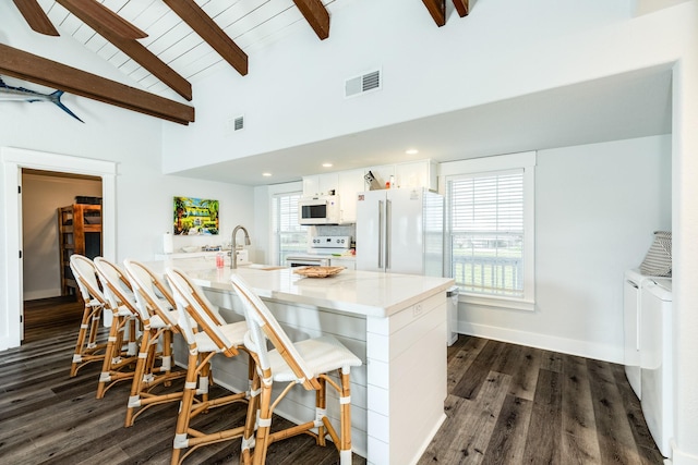 kitchen with white cabinetry, sink, a kitchen bar, washing machine and clothes dryer, and white appliances