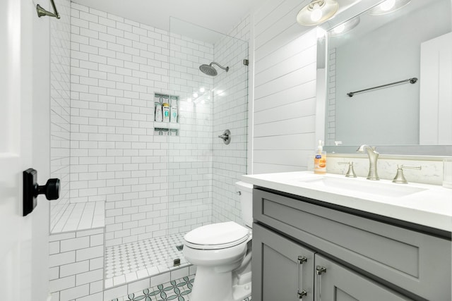 bathroom with vanity, wooden walls, toilet, and tiled shower