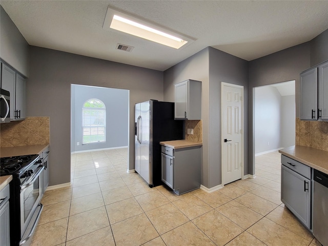 kitchen with appliances with stainless steel finishes, gray cabinetry, backsplash, light tile patterned floors, and a textured ceiling