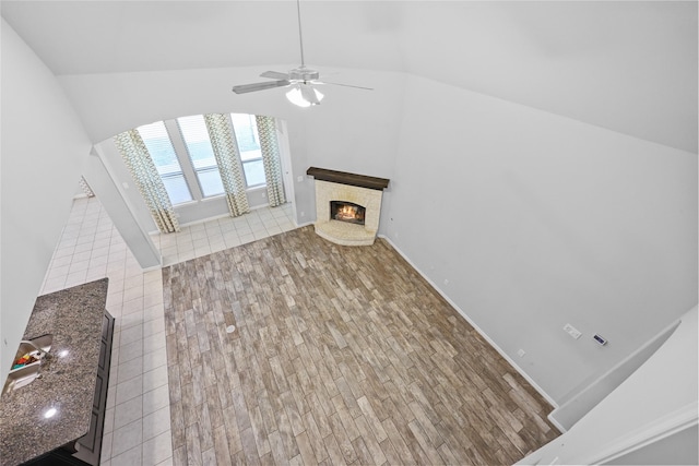 unfurnished living room featuring ceiling fan, tile patterned floors, a fireplace, and vaulted ceiling