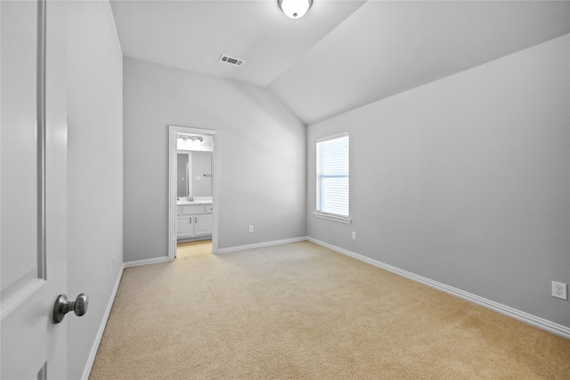 unfurnished bedroom featuring light carpet, vaulted ceiling, and ensuite bathroom