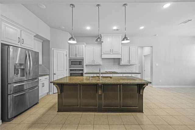 kitchen with appliances with stainless steel finishes, dark stone counters, a center island with sink, and white cabinets